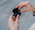 Man taking out a black wireless earbud from charging box outdoors